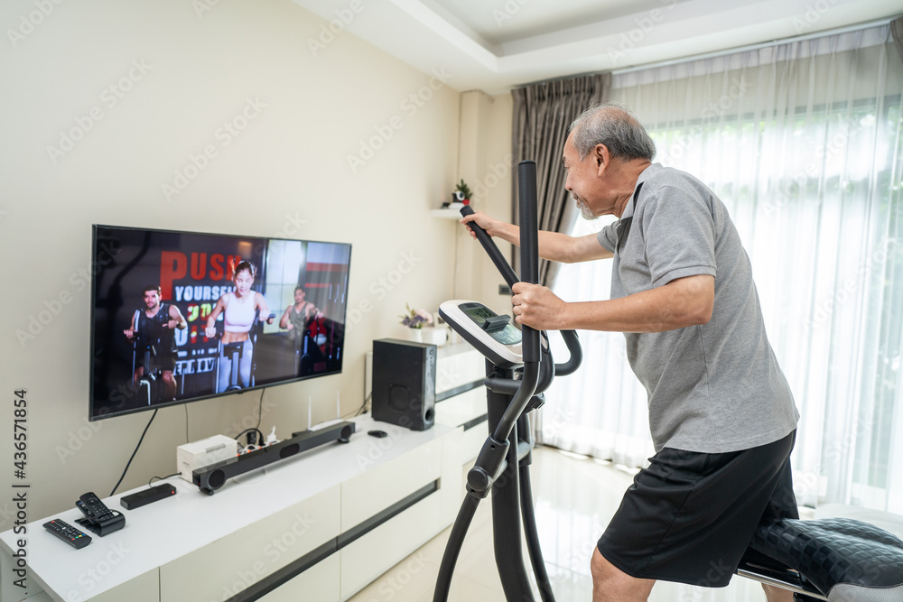 Senior old man use exercise bike machine, follow workout video at home