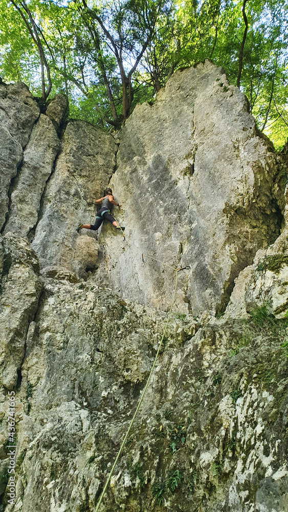 垂直：一名寻求肾上腺素的年轻女子在阳光明媚的森林中爬上悬崖。