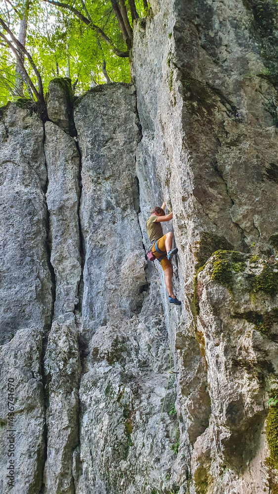 垂直：一个寻求肾上腺素的年轻人在宁静的森林中爬上悬崖。