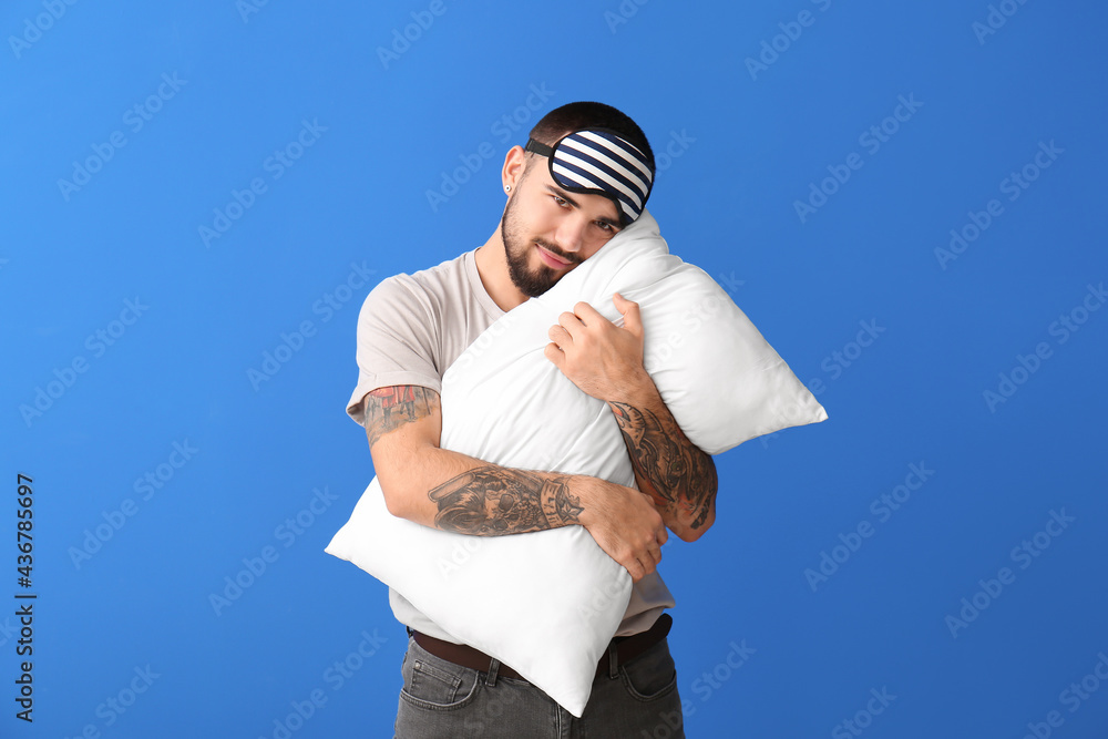 戴着睡眠面罩的年轻人在彩色背景上拥抱枕头