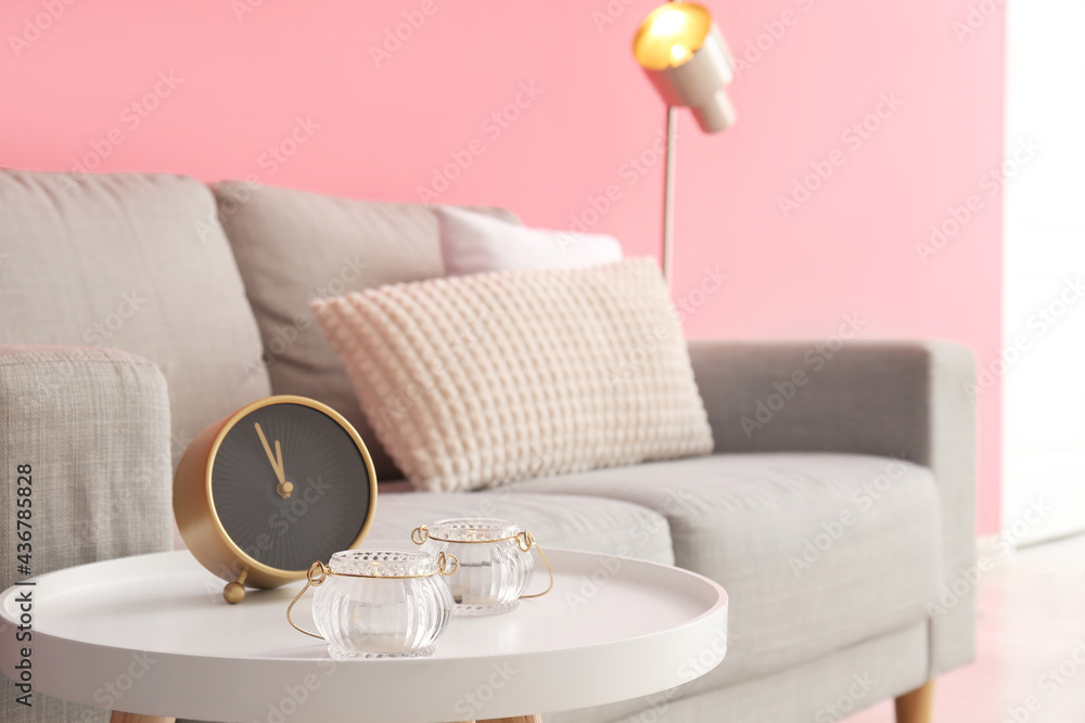 Candles and alarm clock on table in stylish living room