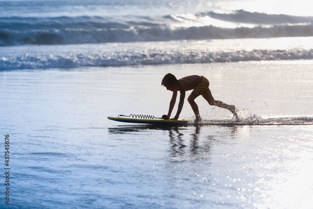 快乐男孩-带着冲浪板的年轻冲浪者在海滩上玩得很开心，在海水池旁跑步。活跃的家庭生活