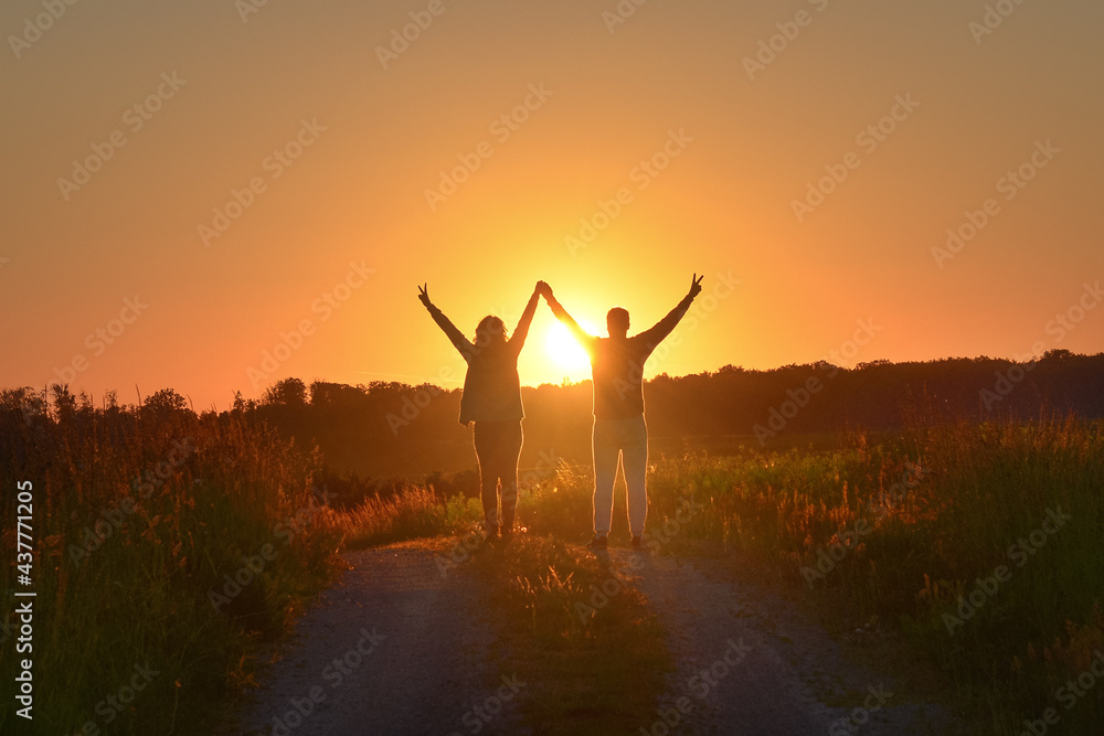 Young couple holding hands towards the Sun and giving the victory sign