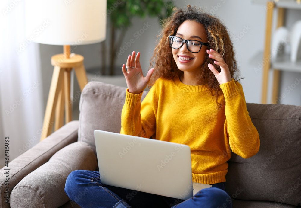 Surprised afro american woman having video call while working or studying online on sofa at home