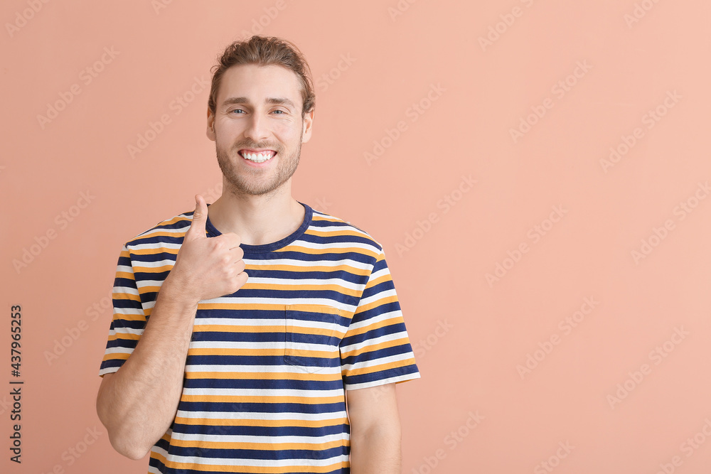 Smiling young man showing thumb-up on color background