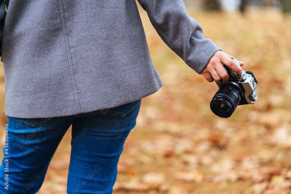 近距离女性旅行者一手拿着相机站在秋天棕色的落叶树上