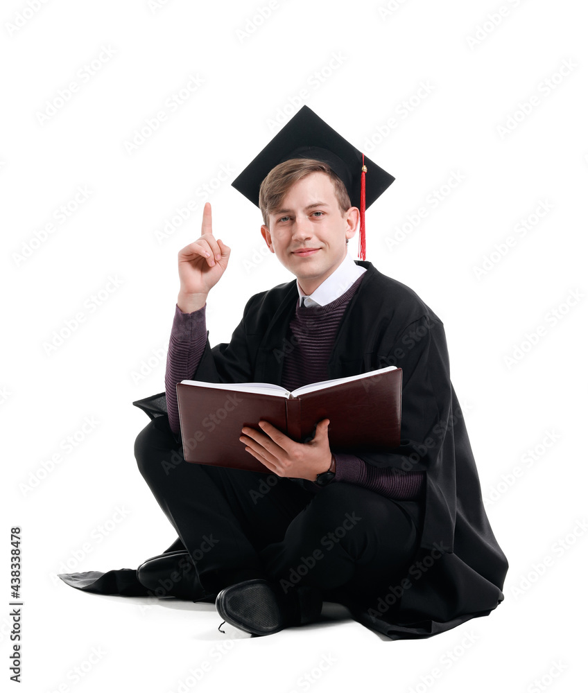Male graduating student with book and raised index finger on white background