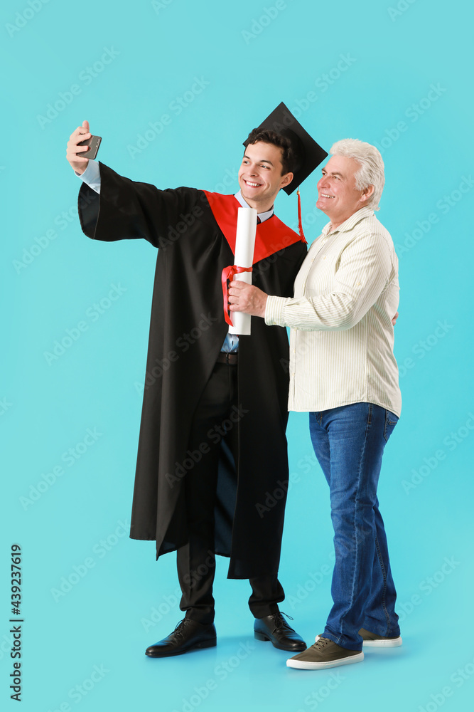 快乐的男毕业学生和他的父亲在彩色背景下自拍