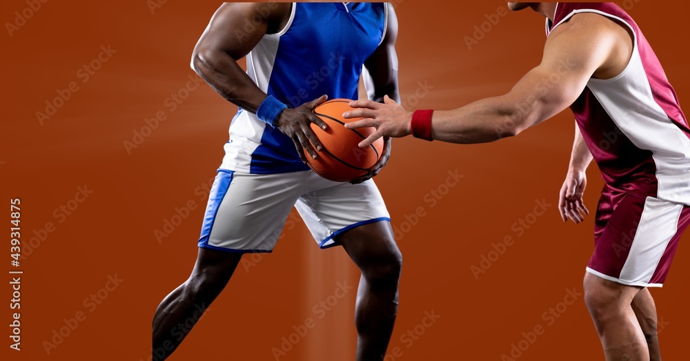 Mid section of two diverse male basketball players playing against spot of light in background