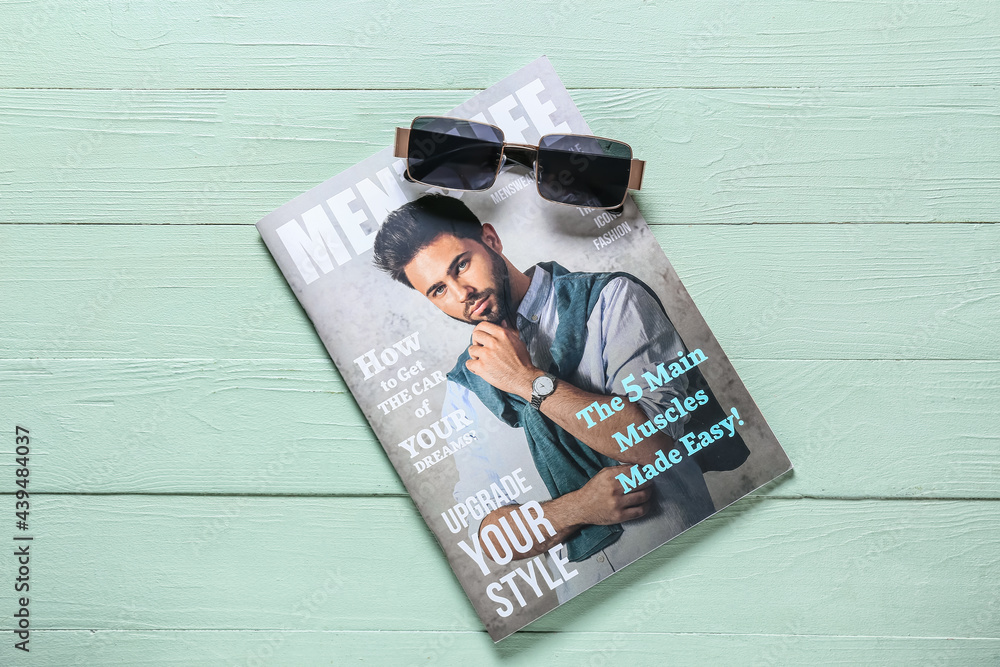 Stylish male sunglasses with fashion magazine on color wooden background
