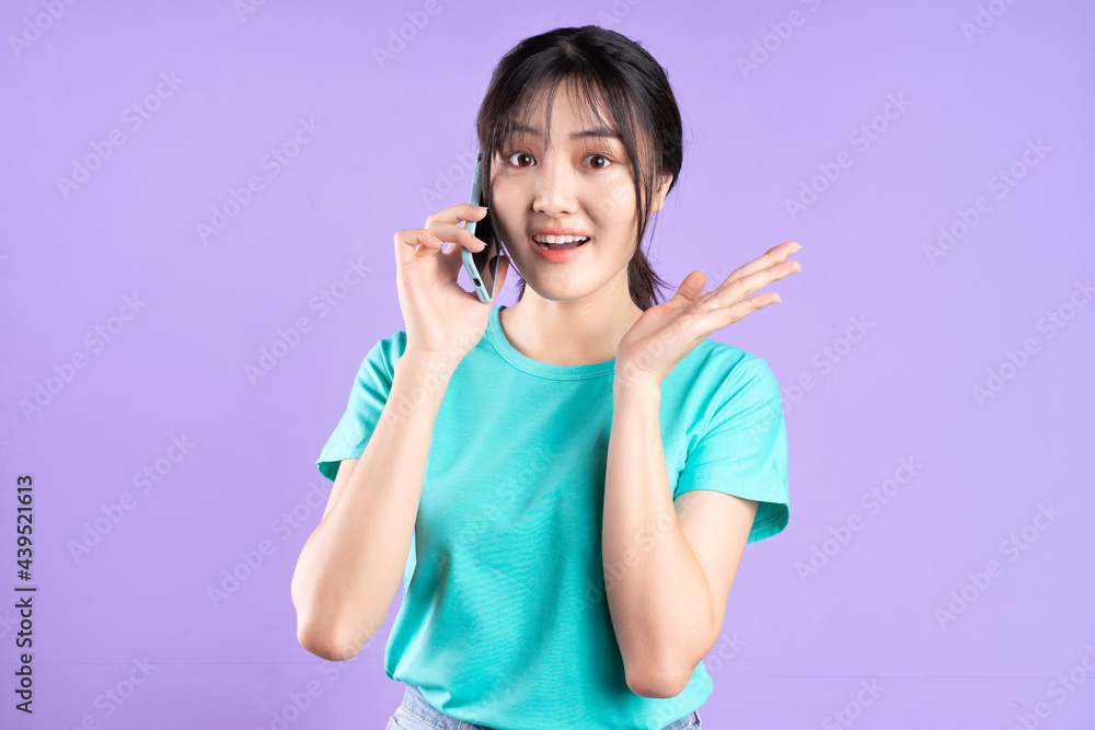 身穿青色衬衫的年轻亚洲女孩在紫色背景下使用手机