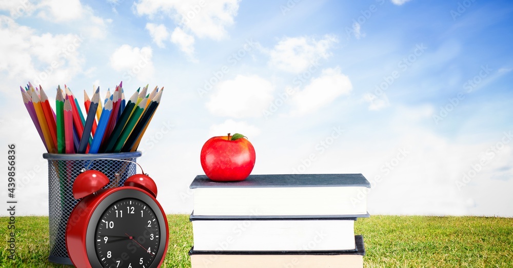 苹果在一叠书、闹钟和铅笔架上，背靠草地和蓝天