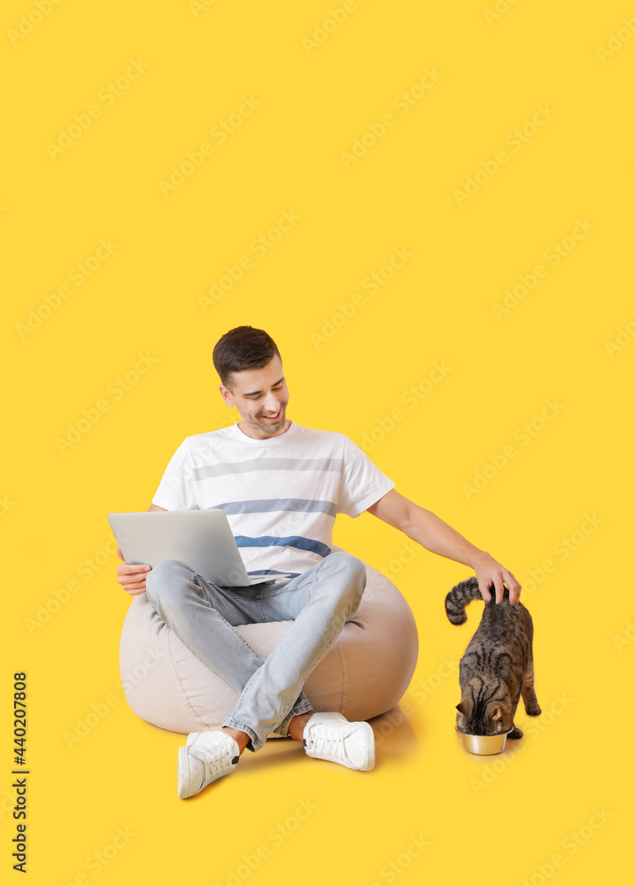 年轻人带着可爱的猫在彩色背景上使用笔记本电脑