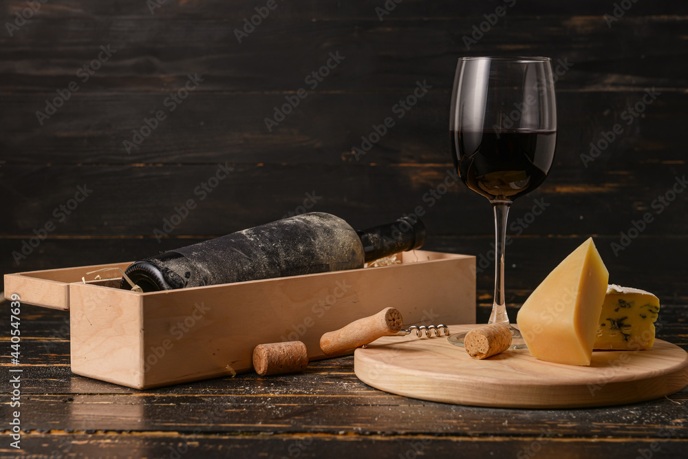 黑色木质背景上装有葡萄酒、奶酪和玻璃杯的盒子