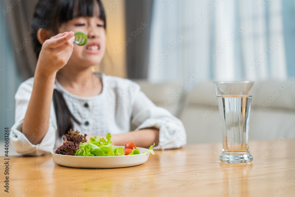 Unhappy Asian girl child dont want to eat vegetables on dinner plate.