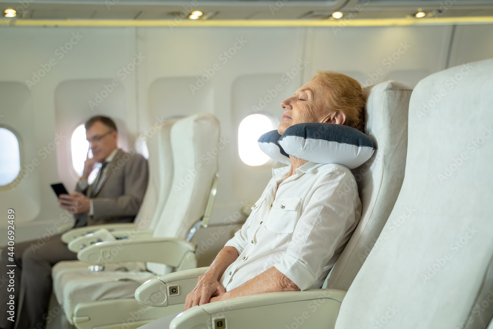 老年女乘客在客舱飞机飞行过程中睡觉。