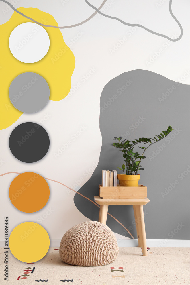 房间彩色墙附近的桌子，有室内植物、书籍和脚凳。不同的颜色图案