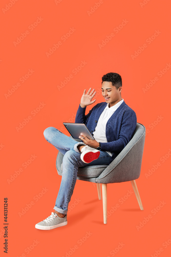 年轻的非裔美国人拿着平板电脑坐在彩色背景的扶手椅上