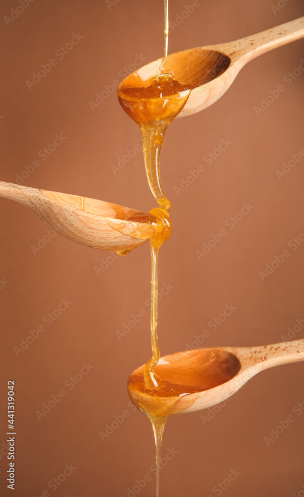 Wooden spoons with dripping honey on color background, closeup