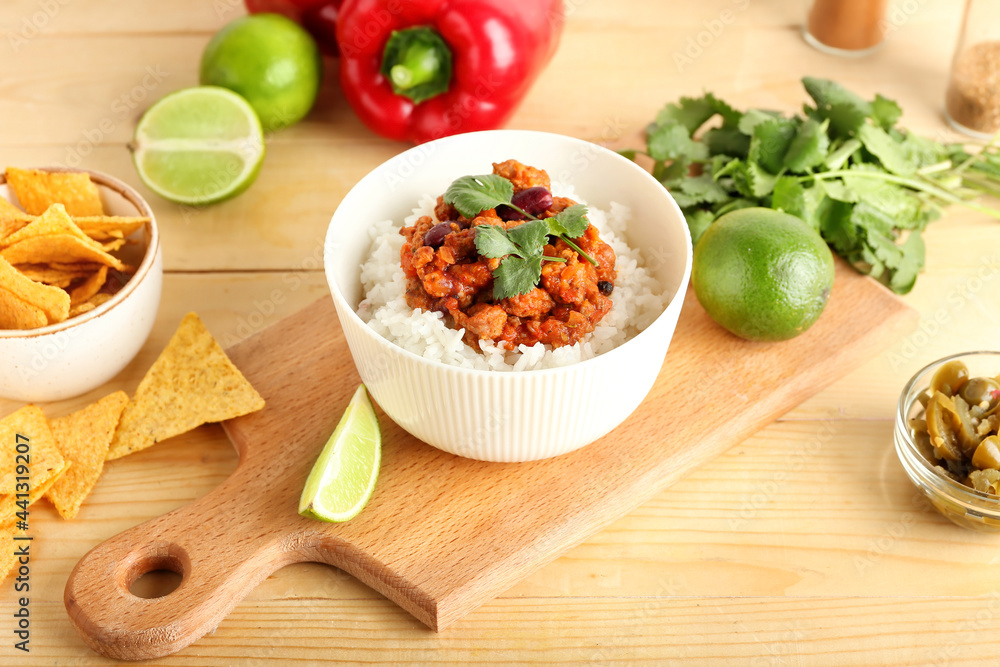 Bowl with tasty chili con carne, rice, lime and nachos on wooden background