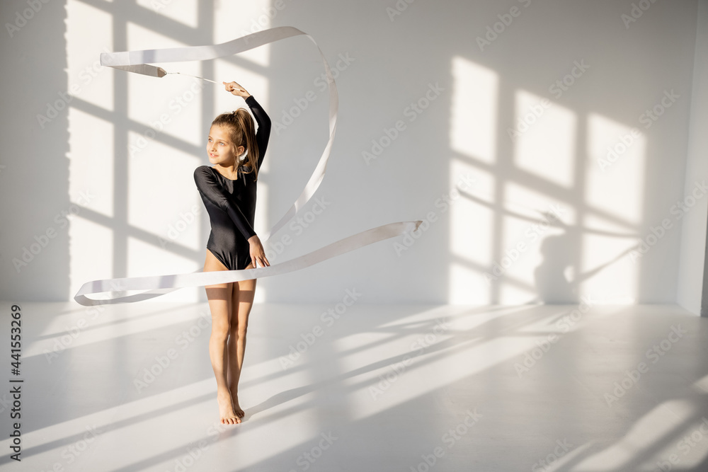 小女孩在阳光明媚的白色舞厅里用体操磁带练习艺术体操。现场直播
