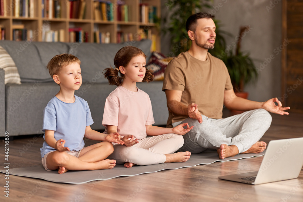 爸爸带着孩子，小儿子和女儿在网上做瑜伽，在地板上摆莲花姿势，冥想