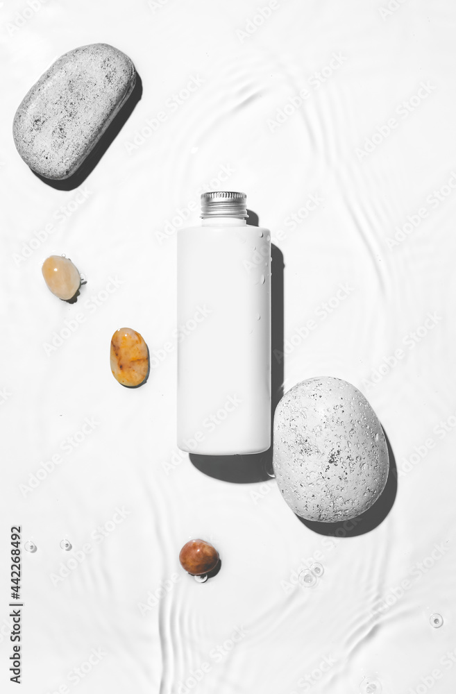 白色背景下的一瓶化妆品和水中的石头