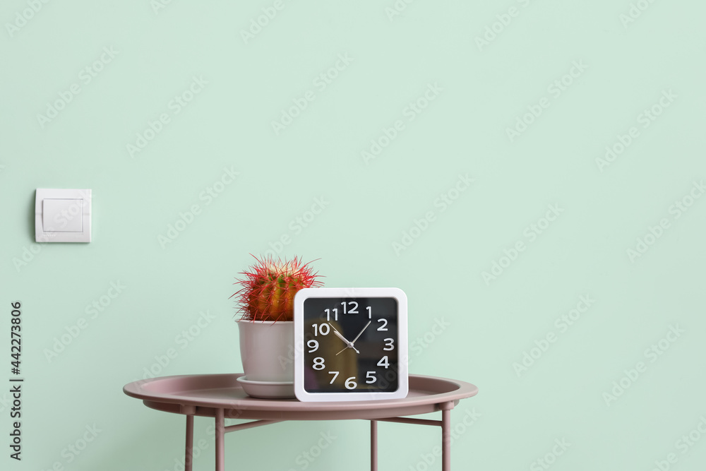 彩色墙附近桌子上的时钟和仙人掌