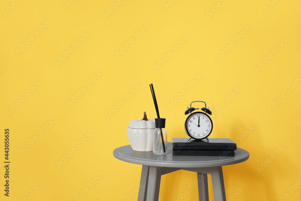 黄色墙壁附近的灰色桌子，里面有书、闹钟和香气清新剂