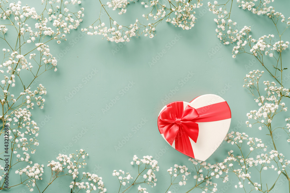 带礼物的鲜花组合。绿松石蓝色背景上的白色花朵和成形的心形礼物。周三