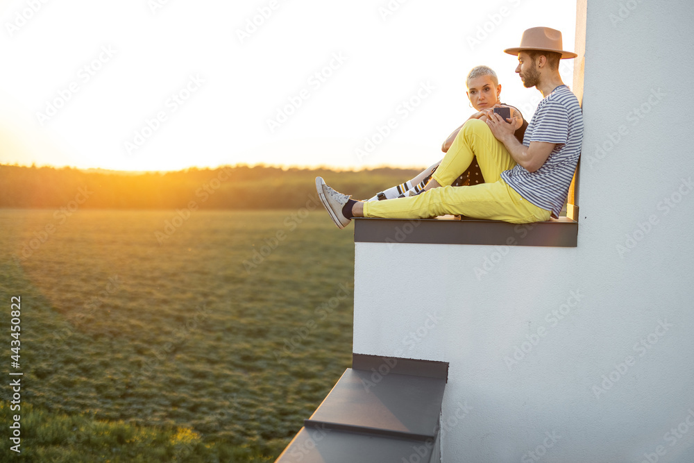 时尚的情侣坐在屋顶上亲密交谈，享受日落美景
