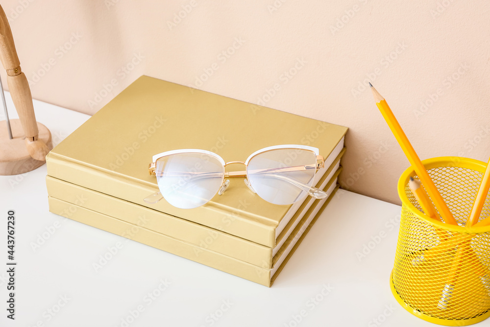 彩色墙附近桌子上有带书和铅笔的时尚眼镜