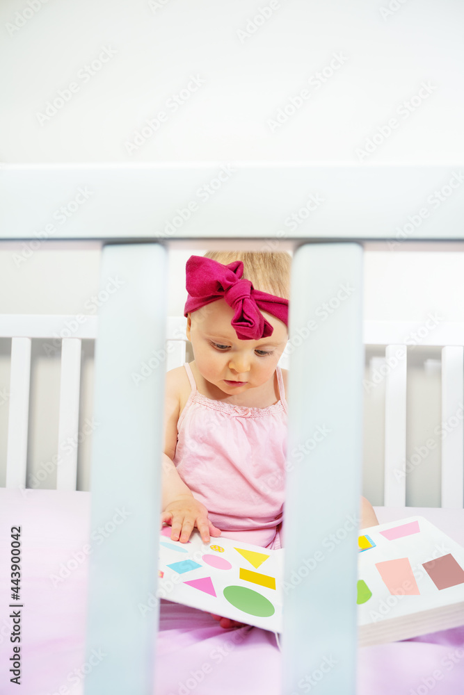 女孩宝宝坐在婴儿床上看形状的书