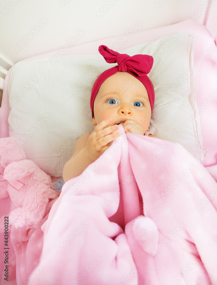 粉色婴儿床上的女婴，带红色蝴蝶结和毯子