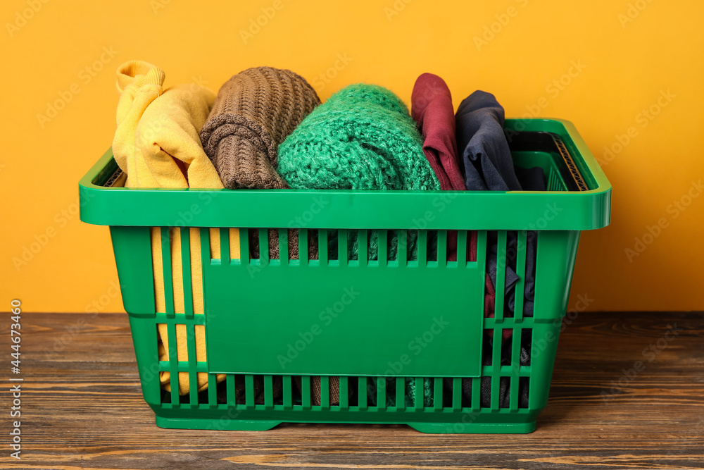 Shopping basket with clothes on table near color wall