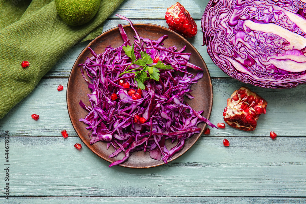 彩色木质背景上有切好的新鲜紫色卷心菜和石榴的盘子