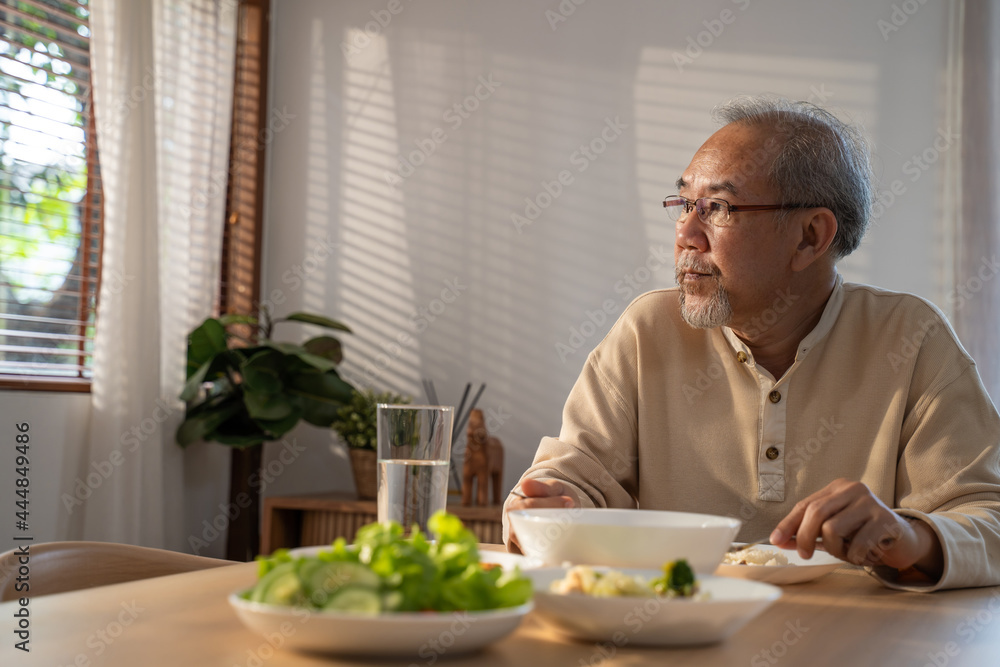 不快乐的亚洲老年人独自坐着，在家里的桌子上吃食物。