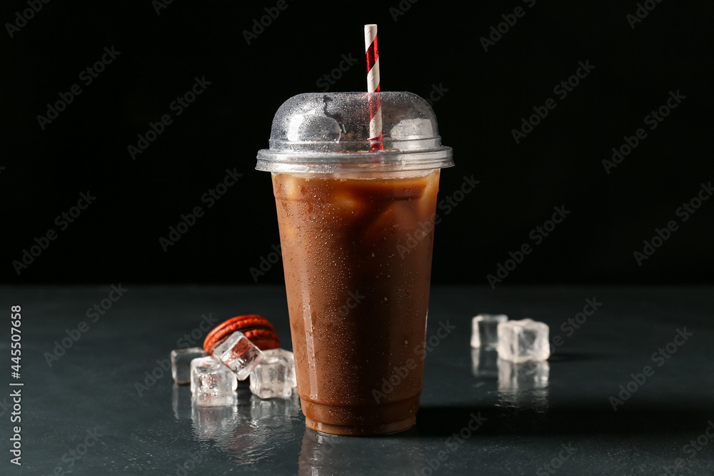深色背景上有咖啡和冰块的塑料杯
