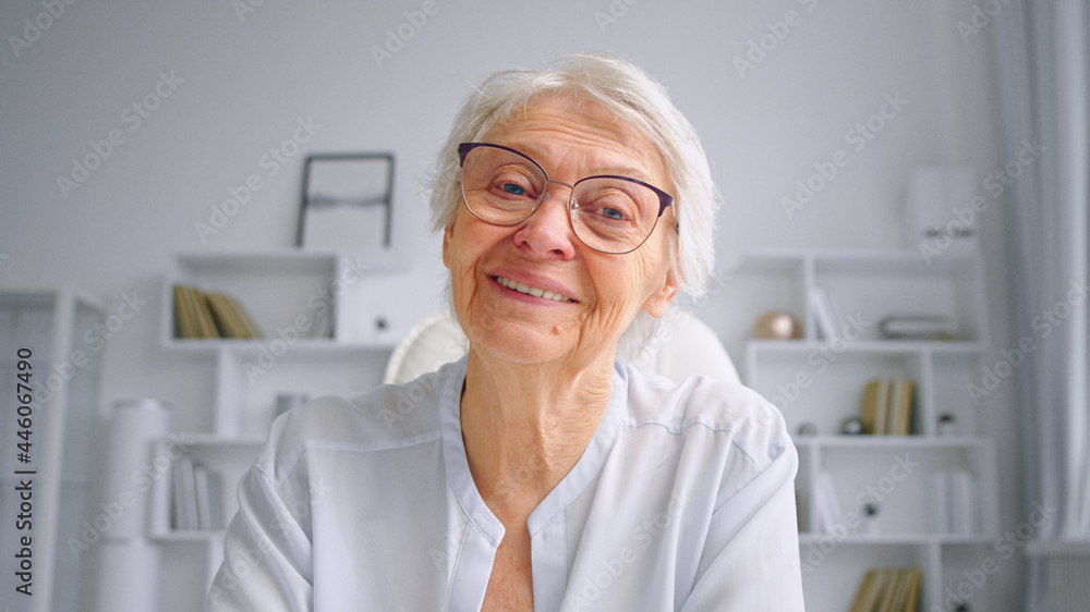 戴着眼镜、头发花白、面带微笑的老母亲挥手问候成年儿童，并在网上聊天