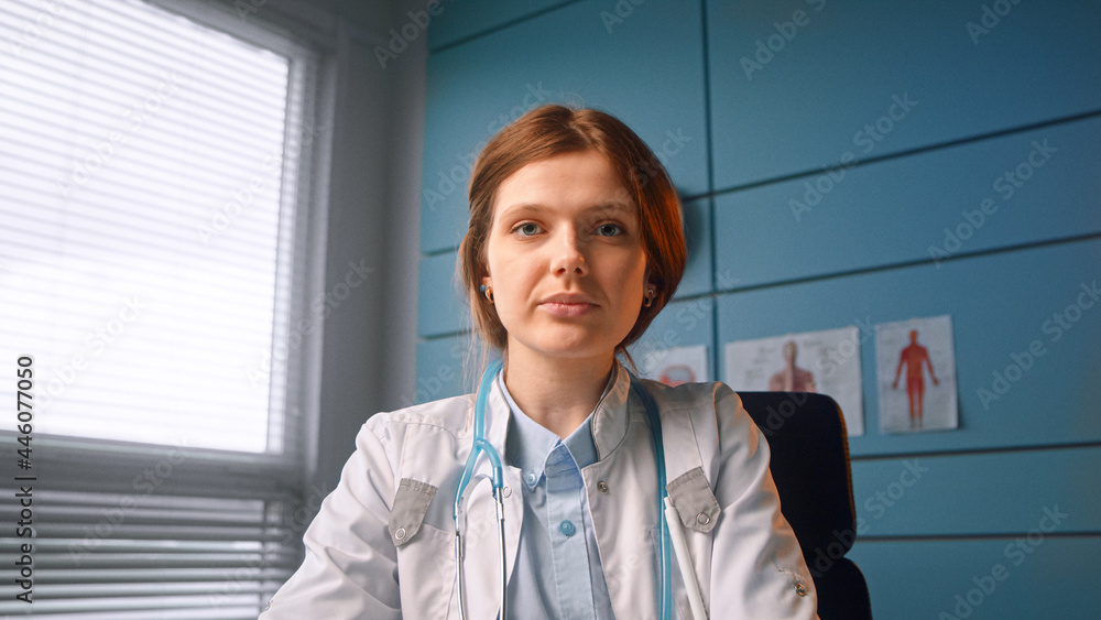 穿着白大褂的布鲁内特医务人员坐在蓝色墙上的办公室里谈论视频通话