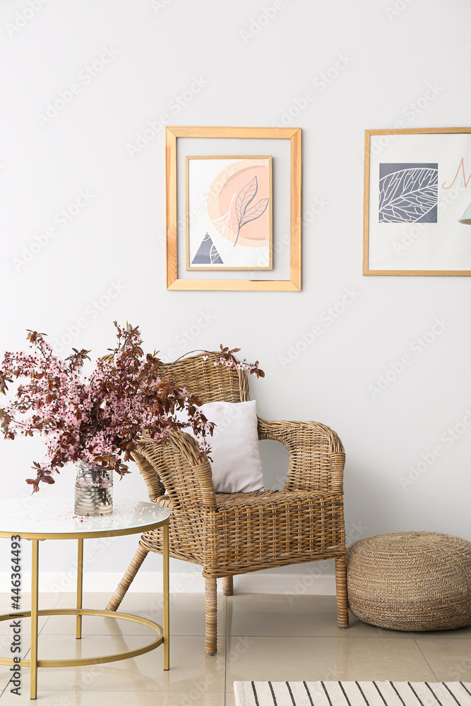 桌子和扶手椅上靠近浅色墙壁的花瓶，上面有开花的树枝