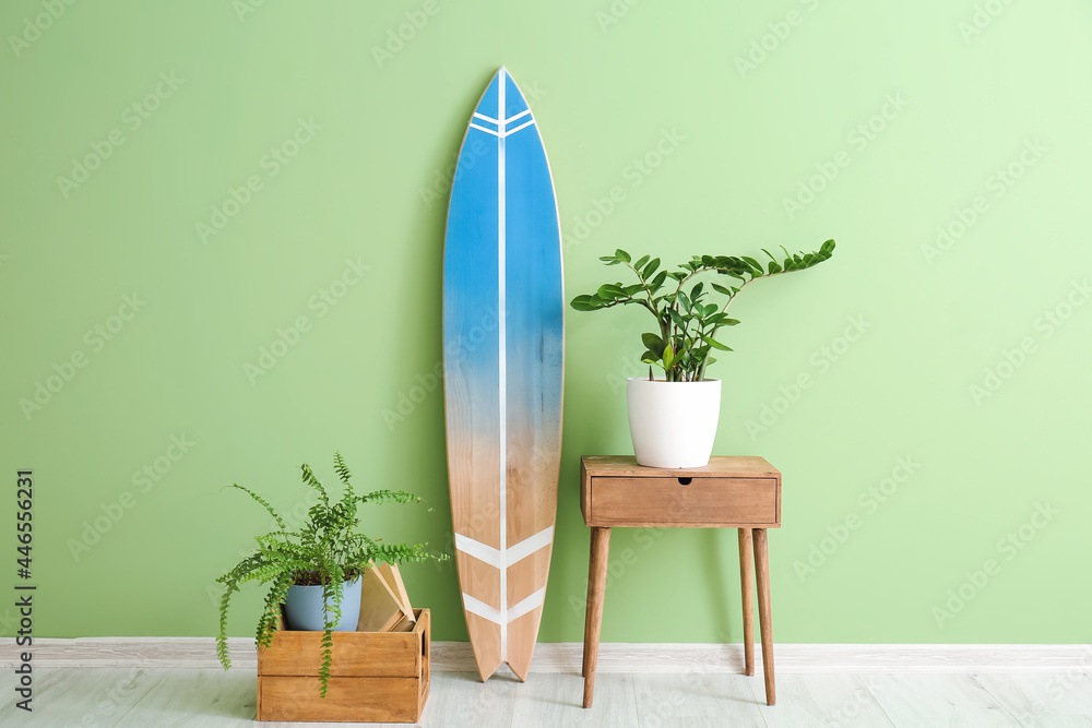 Surfboard, table and houseplants near color wall