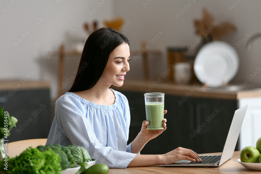 年轻女子在厨房里用笔记本电脑喝着一杯奶昔