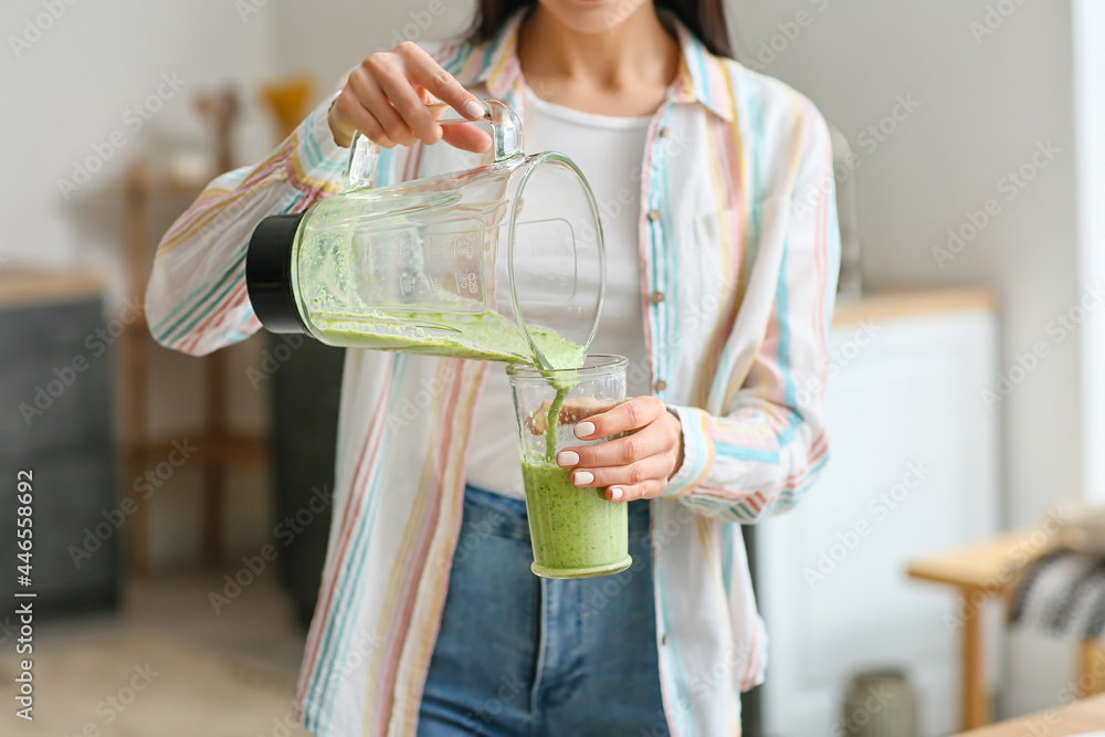 年轻女子在厨房将健康的绿色奶昔倒入玻璃杯