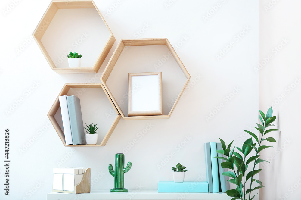 Shelves with books, frame and decor hanging on light wall