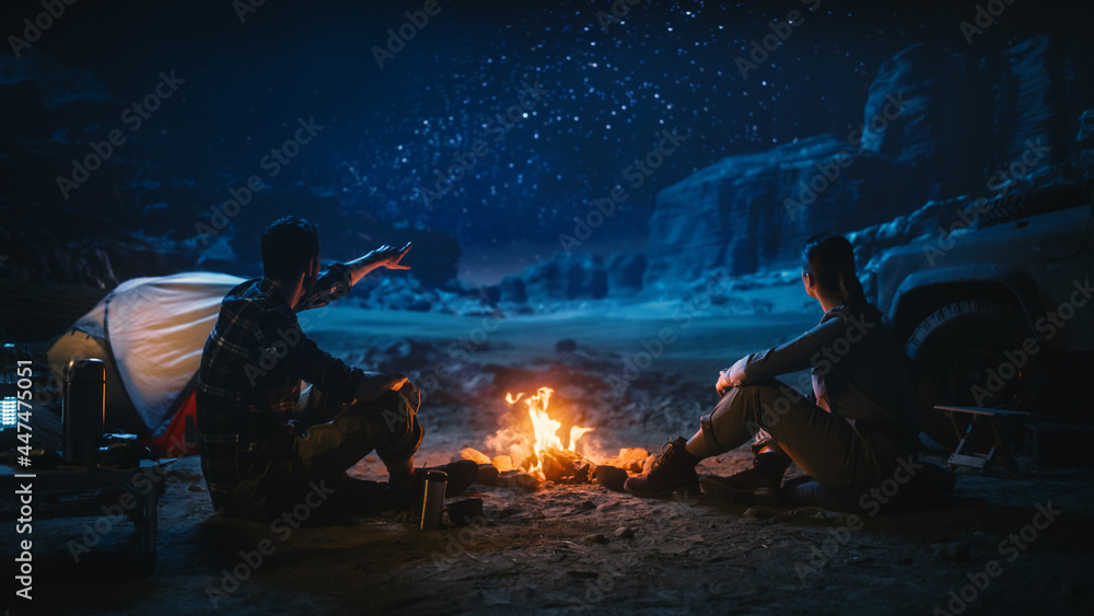可爱的年轻情侣在峡谷露营时坐在篝火旁看夜空。女朋友a