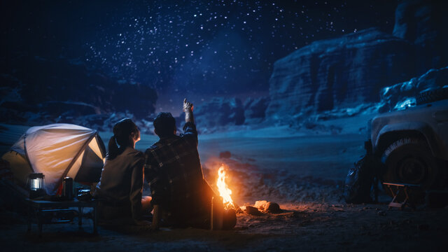 快乐的夫妇自然露营在峡谷，坐在一起看篝火，聊天，看黑