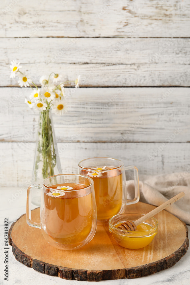 浅木背景上的美味洋甘菊茶、鲜花和蜂蜜的玻璃杯
