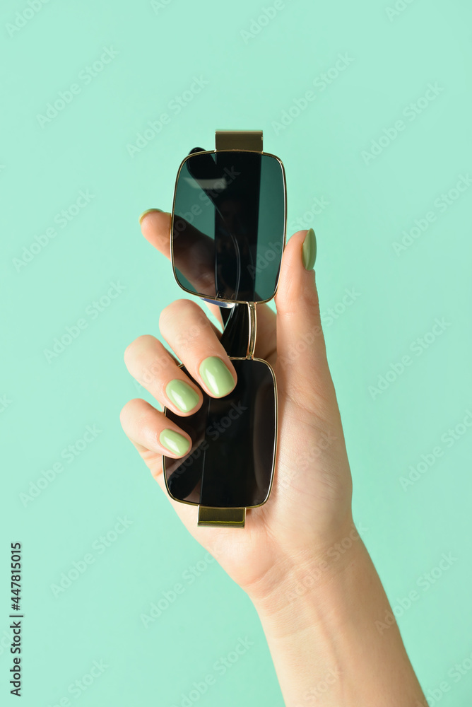 Female hand with sunglasses on color background