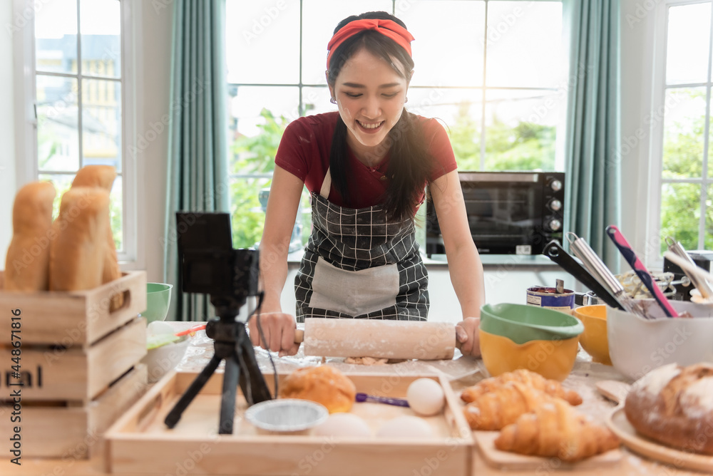 快乐的亚洲女人正在烹饪饼干，在厨房里玩得很开心。她正在为她的culinar制作视频